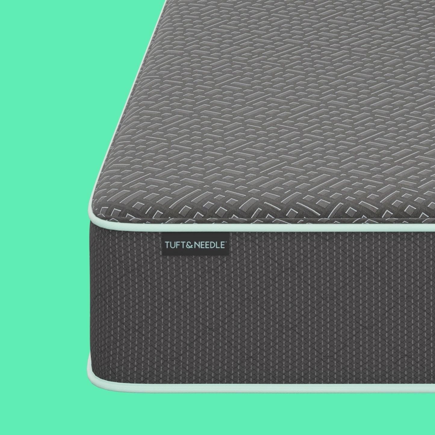 Close-up corner view of a the Tuft and Needle 13.5" Mint Hybrid II mattress showing a dark gray textured top surface and side panel with a visible TUFT & NEEDLE label, set against a solid mint green background.