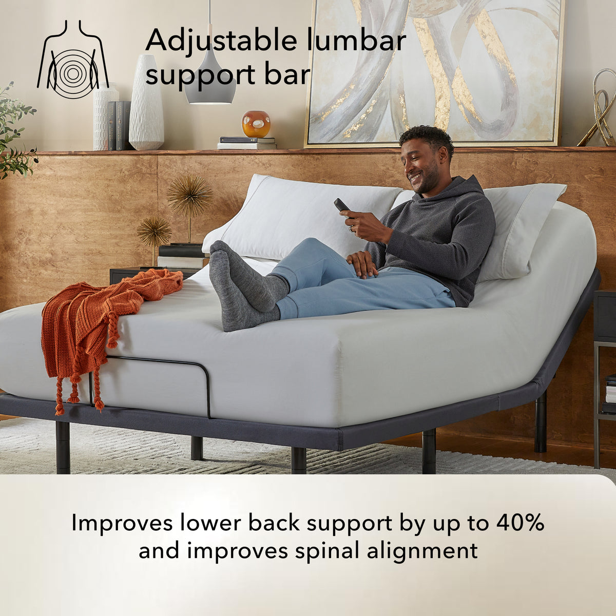 Man using a smartphone on a bed on a Baselogic Pearl adjustable base lumbar support bar highlighted.