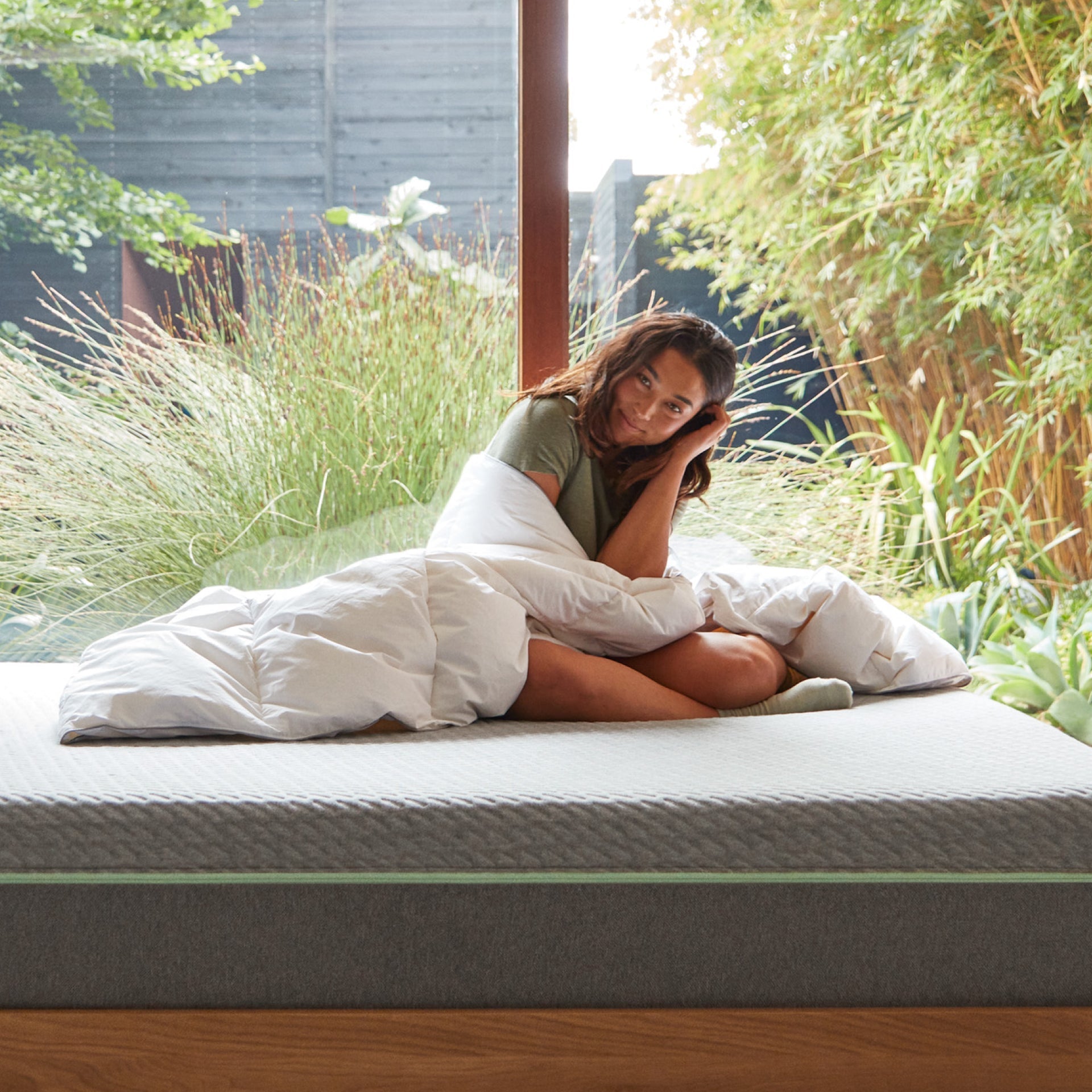 A woman sitting on a bed wrapped in the Tuft and Needle Alternative Duvet Insert||weight:light