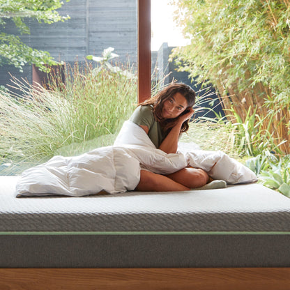 A woman sitting on a bed wrapped in the Tuft and Needle Alternative Duvet Insert||weight:light