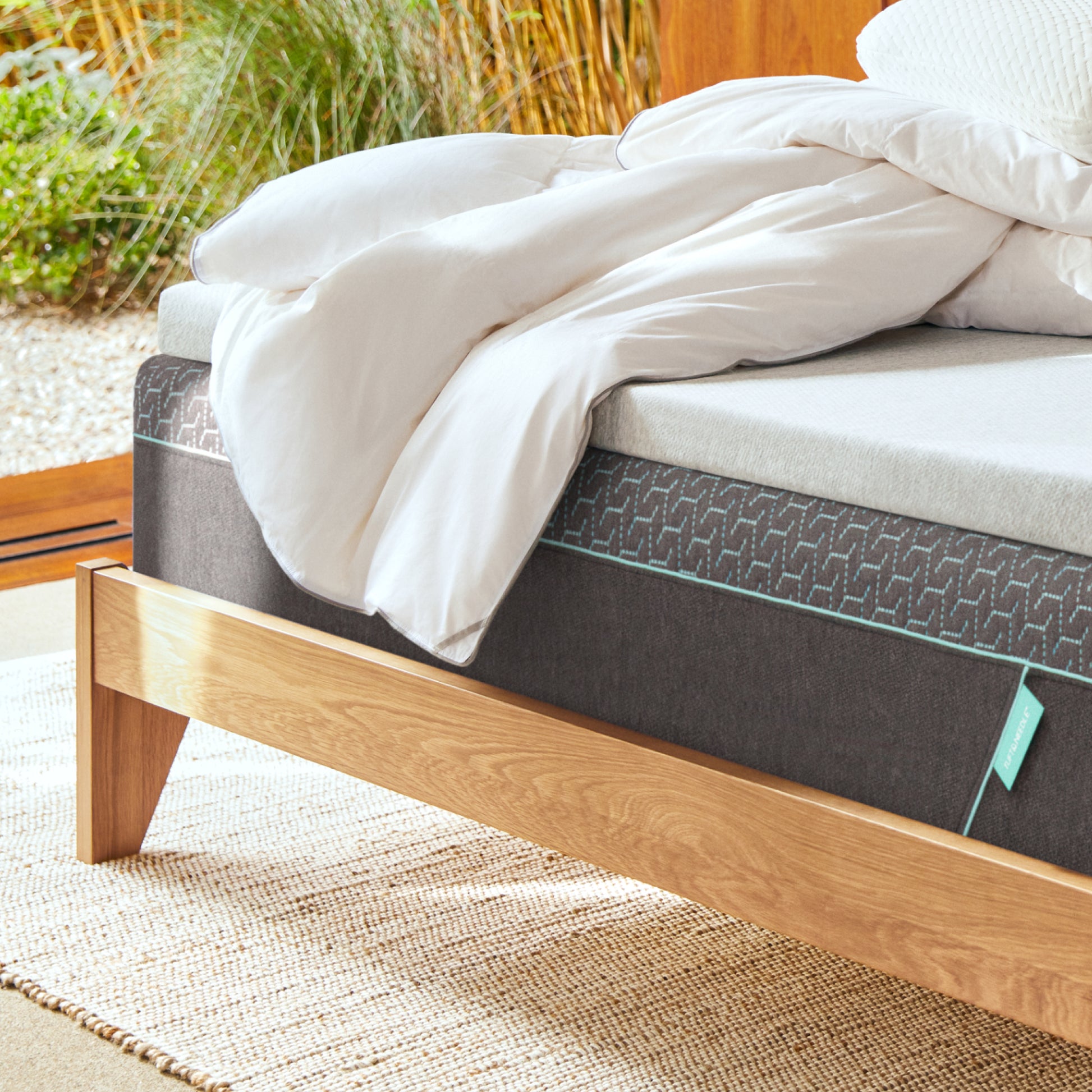 Tuft and Needle Mattress on a wooden bed frame with white down duvet insert on top with an outdoors background