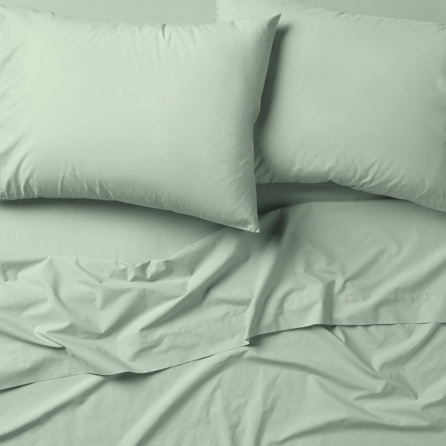 The Tuft and Needle Classic Percale Sheet Set, 2 pillows on top of a sheet on a mattress || color: Sage
