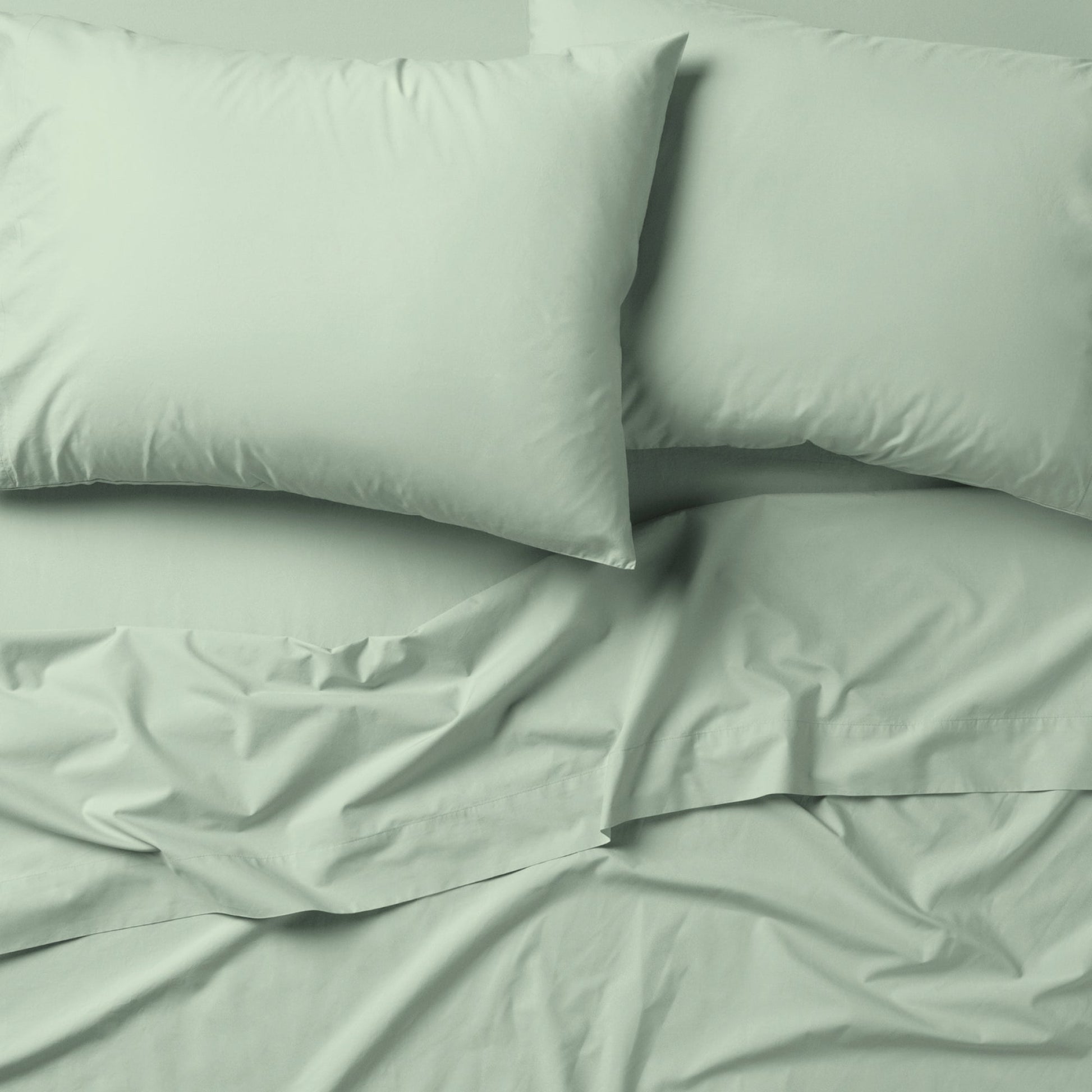 The Tuft and Needle Classic Percale Sheet Set, 2 pillows on top of a sheet on a mattress || color: Sage
